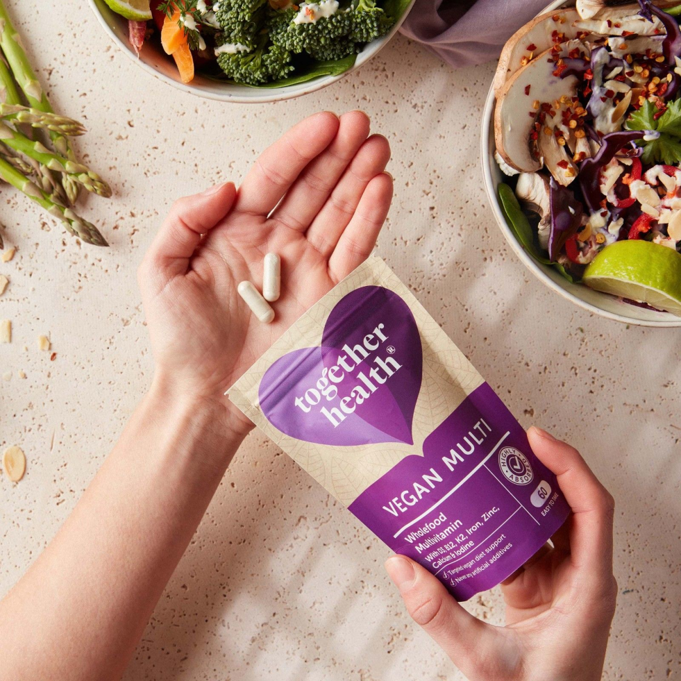 Close-up of Together Health Vegan Multi wholefood multivitamin pack held in hand with capsules, plant-based supplement for daily wellness.